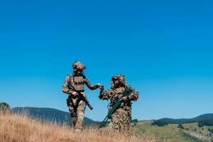 une tireur d'élite équipe équipe de soldats est Aller à l'abri. tireur d'élite assistant et équipe chef en marchant et visée dans la nature avec Jaune herbe et bleu ciel. tactique camouflage uniforme. photo