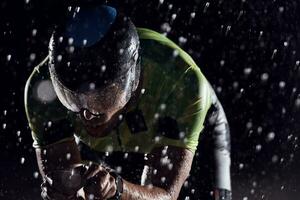 athlète de triathlon faisant du vélo rapidement la nuit pluvieuse photo