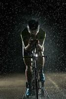athlète de triathlon faisant du vélo rapidement la nuit pluvieuse photo