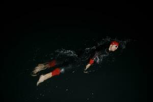 athlète de triathlon nageant dans la nuit noire portant une combinaison de plongée photo