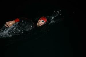 athlète de triathlon nageant dans la nuit noire portant une combinaison de plongée photo