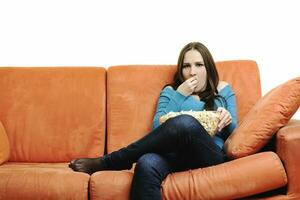 jeune femme mange du pop-corn sur un canapé orange photo