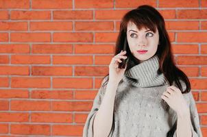 une jolie fille parlant par téléphone portable, yeux surpris, en pull gris photo