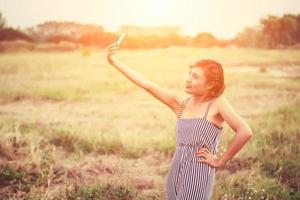 jeune femme debout à l'aide de son smartphone selfie dans le champ d'herbe. photo