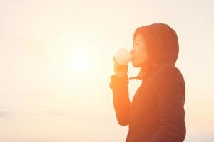 jeune femme buvant une tasse de café avec le lever du soleil le matin.