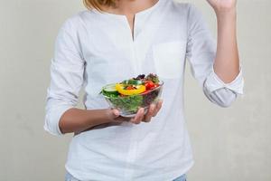 mains de belle femme tenant un grand bol de salade de légumes frais. photo