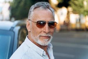 Portrait d'homme senior à l'extérieur dans une chemise et des lunettes de soleil photo