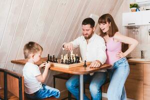 Enceinte maman en train de regarder papa et fils jouer échecs à le table photo