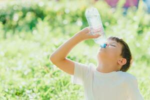 mignonne enfant les boissons l'eau de une bouteille sur le rue dans été photo