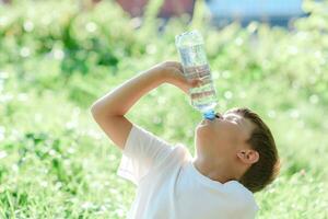 mignonne enfant les boissons l'eau de une bouteille sur le rue dans été photo