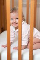 portrait de une en riant peu fille qui est dans une lit de bébé photo