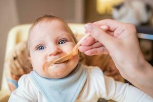 mère alimente content peu fille fruit purée de une cuillère. premier nourriture photo