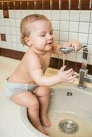 en riant peu fille prend hygiène procédures dans le lavabo dans le cuisine photo