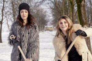 Jeune femmes pelleter neige près une petit bois photo