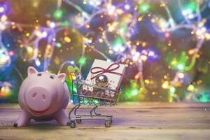 achat, achats Noël cadeaux, présente. dépôt argent pour Noël vacances. Noël porcin banque et achats Chariot plein avec cadeau boîte et Noël jouets. économie argent sur Noël présente photo
