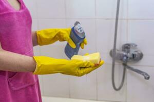 femme dans gants en mettant nettoyage chimie à le éponge et vouloir à nettoyer en haut le salle de bains photo