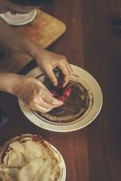 une peu garçon avec le sien mère en train de préparer ensemble une petit déjeuner. mère et fils barbouillage Chocolat crème à mince Crêpes. gratuit espace photo