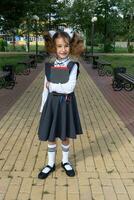 fille avec sac à dos, école uniforme avec blanc arcs et empiler de livres près école. retour à école, content élève, lourd manuels. éducation, primaire école Des classes, septembre 1 photo