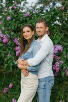 magnifique Jeune couple dans une romantique lieu, printemps épanouissement lilas jardin. content joyeux couple profiter chaque autre tandis que en marchant dans le jardin photo