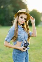 Jeune femme dans une chapeau détient une caméra dans sa mains dans le été en plein air photo