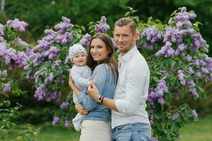 mère, père et peu fils sont en marchant dans une printemps épanouissement parc. une content maman et papa avec une petit enfant sont ayant amusement près le lilas. le concept de une content famille. photo