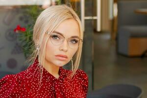 portrait de une magnifique blond femme dans des lunettes et une rouge robe photo