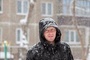 homme dans une capuche pendant une chute de neige. portrait de une homme dans l'hiver. sérieux Regardez photo