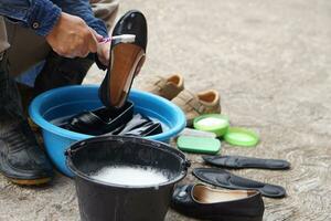 fermer mains utilisation brosse à nettoyer et laver noir des chaussures dans noir seau et bleu bol Extérieur. concept, prendre se soucier, entretien chaussures de saleté et mal odeur pour en utilisant longue temps. hygiène et sanitaire photo