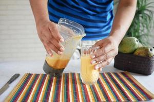 Jeune homme faisant un smoothie à la mangue et un mélangeur sur table photo