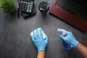 main dans des gants en caoutchouc bleu tenant une table de bureau de nettoyage de flacon pulvérisateur photo