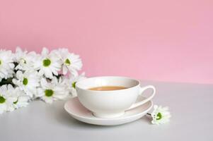 une blanc tasse avec thé et une soucoupe des stands sur une table avec blanc camomille fleurs photo
