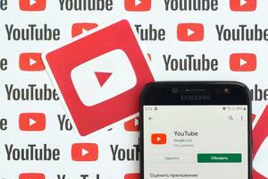 Youtube app sur samsung téléphone intelligent écran sur papier bannière avec petit Youtube logos et les inscriptions. Youtube est Google filiale et américain plus populaire partage de vidéo Plate-forme photo