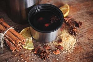 vin chaud dans une tasse avec de la cannelle, du citron sur une planche en bois rustique photo