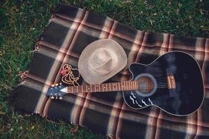 guitare et un chapeau de paille se trouvent sur un plaid sur un fond d'herbe verte
