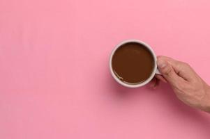 main tenant une tasse de café sur fond rose photo