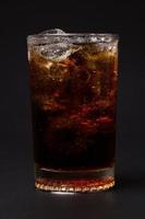 Cola en verre avec des glaçons clairs isolés sur fond noir photo