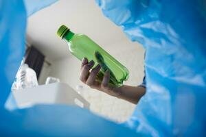 une femme main est lancement une vert Plastique bouteille dans le poubelle peut. photo