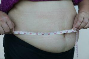 fermer femme mains mesure sa gros ventre, graisse avec cellulite abdomen par en utilisant mesure enregistrer. concept, obésité. en surpoids. corps forme problème pour femme après grossesse ou avoir plus ancien. photo