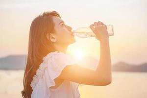belle jeune femme buvant de l'eau avec le lever du soleil le matin photo