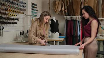 rouleau de tissu gris coupant lentement avec des ciseaux en aluminium sur la table par sud deux femmes tailleurs, créateurs de mode ou couturières travaillant dans un atelier d'atelier