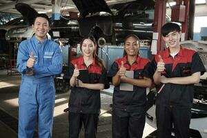 portrait de multiracial professionnel mécanicien équipe les pouces en haut et Regardez à caméra, travail à voiture un service garage, content entretien emplois, vérifier et réparation Occupation dans automobile industrie entreprise. photo