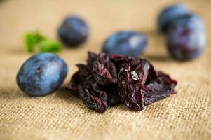 séché pruneaux dans une cuillère sur une toile de jute nappe de table contre une Contexte de Frais prunes. photo