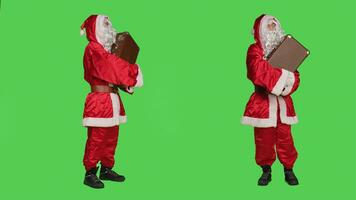 Père Noël claus dans costume avec valise, attendre pour transport plus de plein corps écran vert toile de fond. Jeune homme agissant comme père Noël et porter ancien mallette, vacances concept. photo
