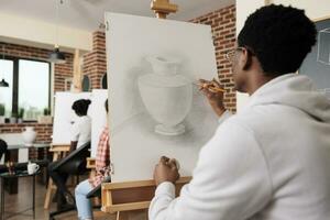 Jeune gens copains assister dessin classe, apprentissage Nouveau compétences ensemble. arrière vue de africain américain étudiant gars esquisse vase avec crayon pendant groupe art leçon. la créativité et découverte de soi photo