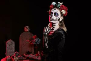 horreur Dame de décès portant noir glamour costume dans studio, à la recherche comme saint Père Noël muerte avec fleurs couronne. agissant terrifiant et posant habillé comme déesse de mort sur dios de los morts. photo