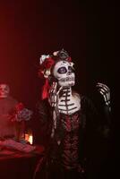 déesse de décès avec sucre crâne faire en haut parlant sur téléphone appel, en utilisant téléphone intelligent à bavarder dans studio. femme célébrer dios de los muertos vacances avec la cavalera catrina costume, saint festival. photo