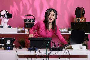 asiatique musicien en jouant électronique la musique en utilisant professionnel platines tandis que permanent à dj table dans studio plus de rose Contexte. artiste Faire performance à boîte de nuit avec l'audio équipement photo