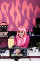 vlogger avec rose cheveux et T-shirt montrant carnet recommandation révision école produit dans de face de caméra tandis que tournage vlog. asiatique influenceur en utilisant professionnel diffuser équipement photo