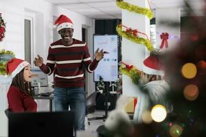 diverse affaires équipe profiter café Pause à travail, ayant amusement ensemble dans de fête orner Bureau pendant vacances saison. collègues sentiment Noël esprit humeur, relaxant dans Noël fleuri espace de travail photo