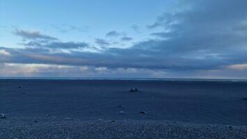 islandais en bord de mer réglage à le coucher du soleil avec rosé ciel et glacial pâturages, noir le sable plage offre pittoresque vue. paysage autour énorme ouvert l'eau dans islandais environnement. photo